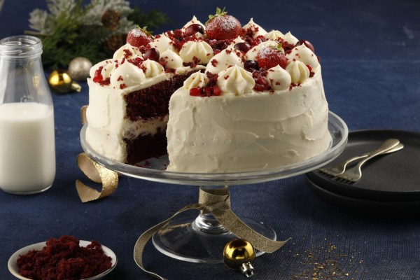 Triple-layer red velvet cake with cream cheese frosting, decorated with cake crumbs and fresh berries.