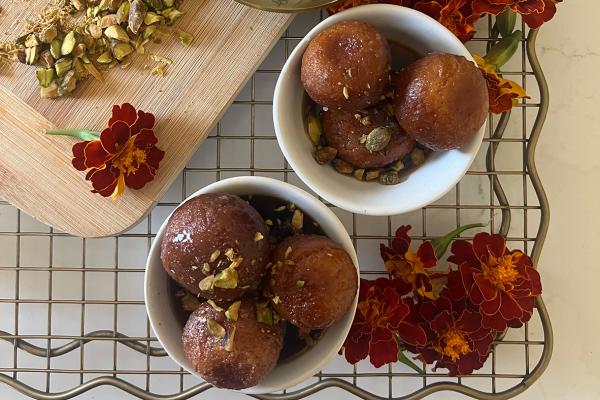Three golden gulab jamun dumplings soaking in fragrant rosewater syrup made with Canadian dairy milk.