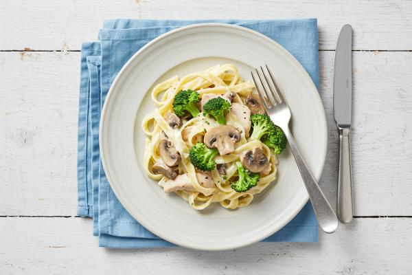 Top-down image of fettuccine alfredo with chicken, mushrooms, and broccoli on a plate
