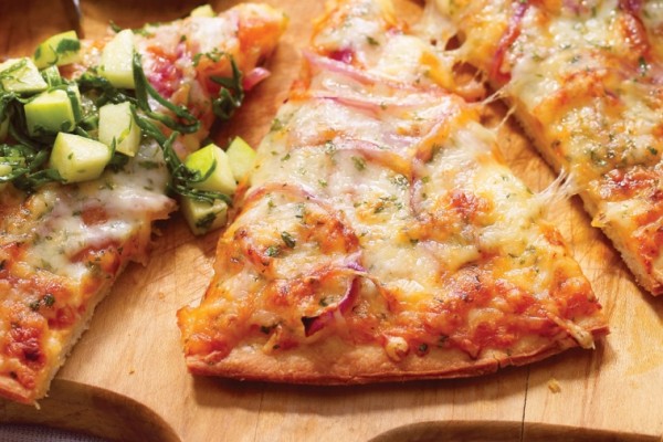 A freshly baked slice of pizza with melted Swiss cheese, topped with a zesty green salad, served on a wooden board for a tasty meal.