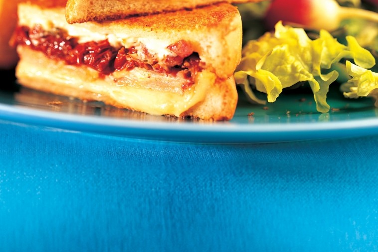 Close-up of halved grilled cheese sandwich with ham, mustard, cheese, and pickle, a modern take on comfort food